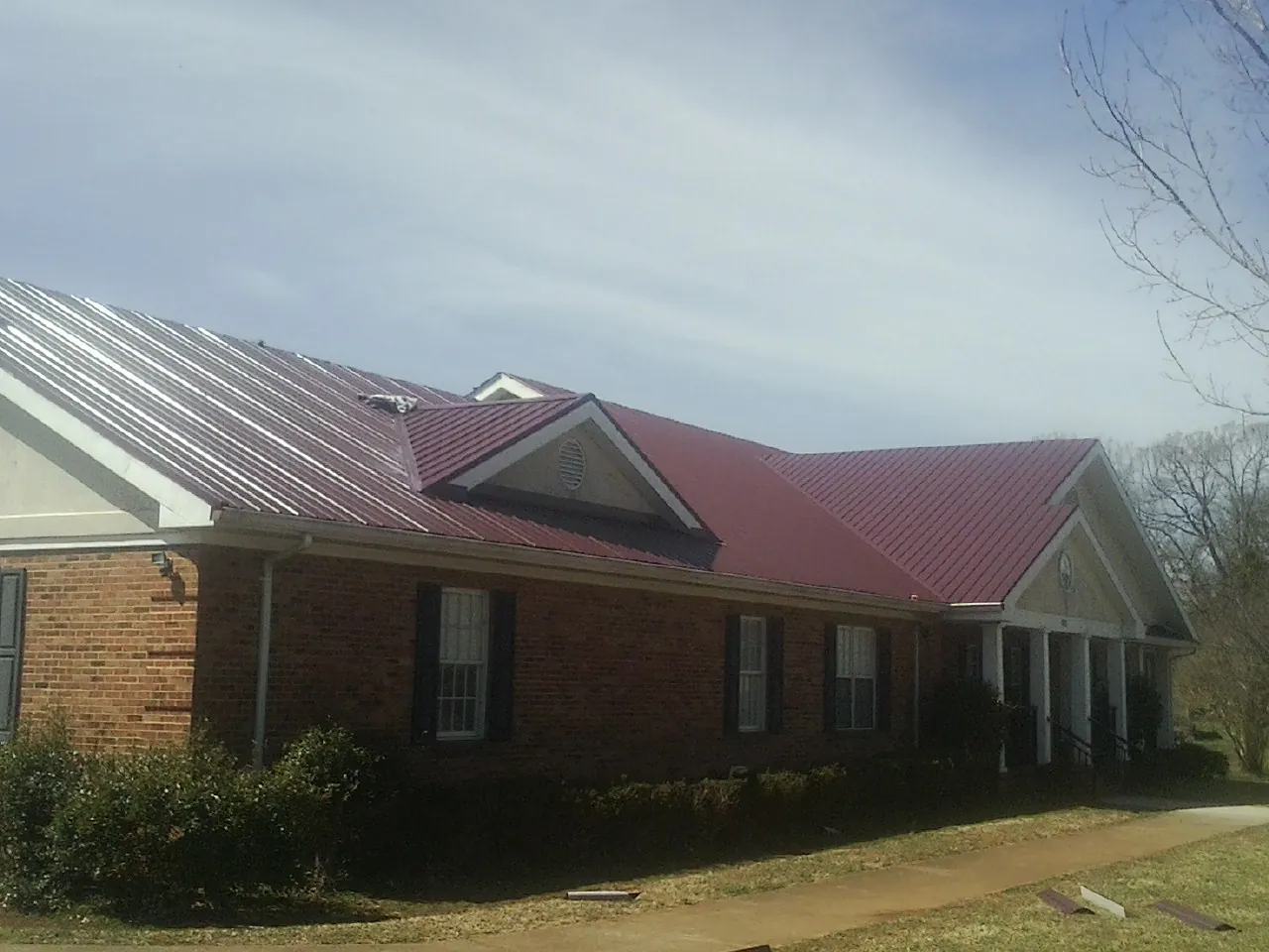 Red metal roof with gabled entries on a long brick building, from a Hail Damage Roof Repair job in Bonners Ferry