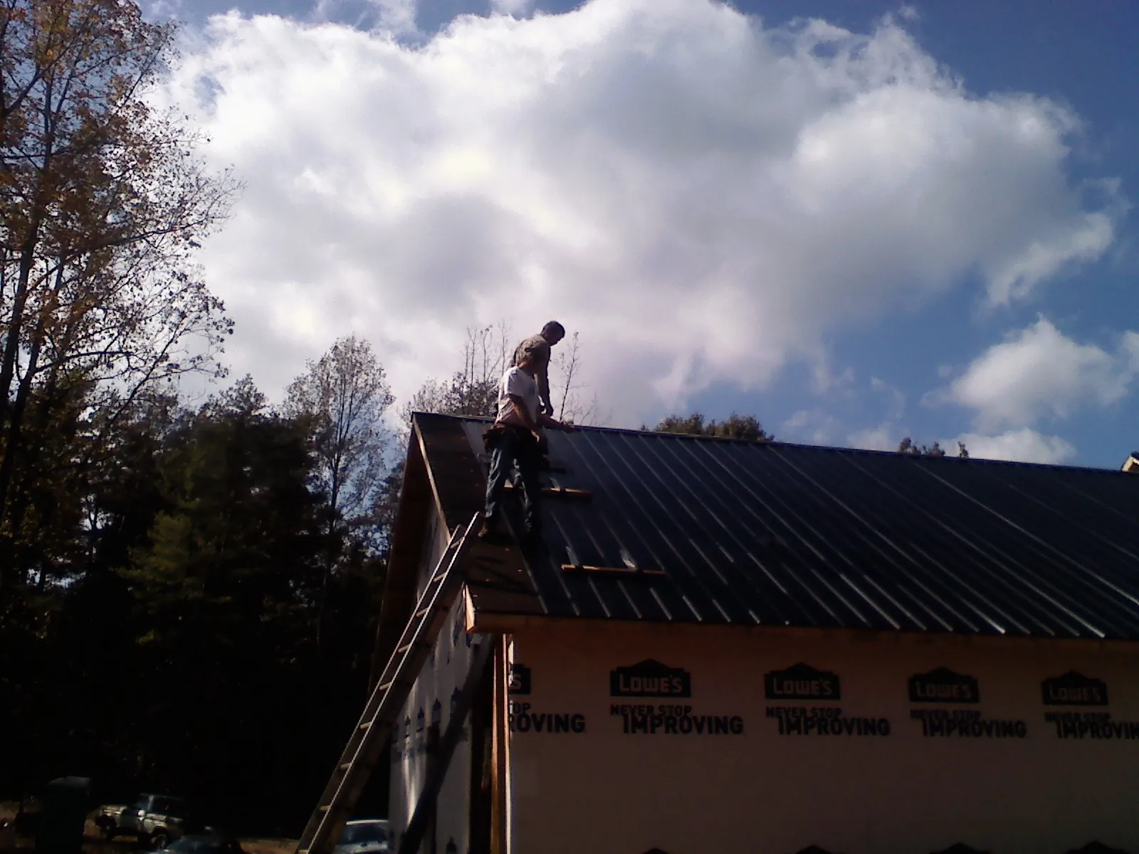 Roofer fastening dark metal panels high against a cloudy sky, from a Roof Inspection job in Bonners Ferry