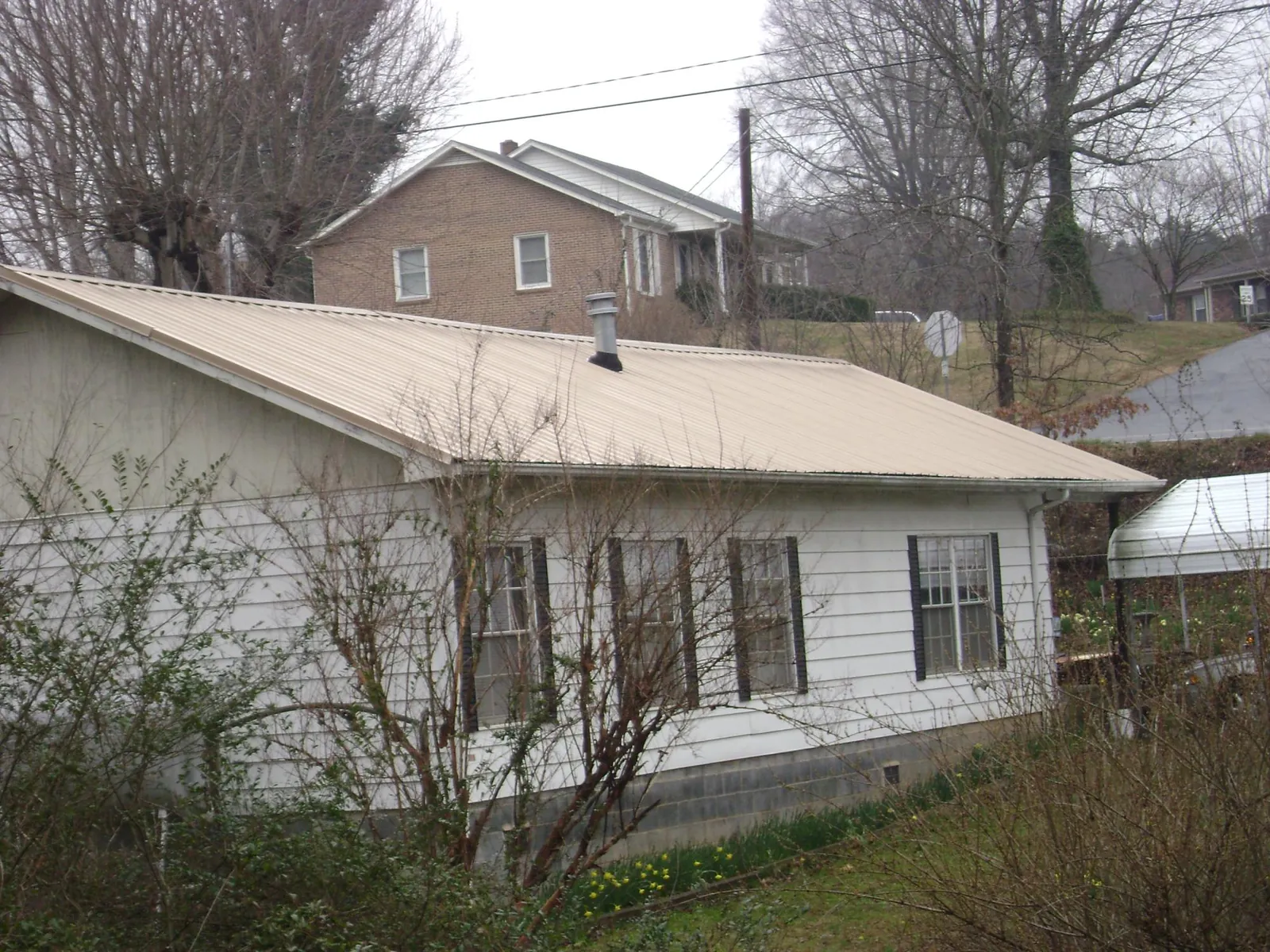 Tan metal roof on a white sided house set into a hillside — Commercial Roofing by Roofing Brothers in Bonners Ferry